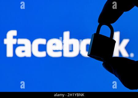 Fingers hold a closed security lock on the background of the facebook social network logo. The concept of data security in Facebook. Stock Photo
