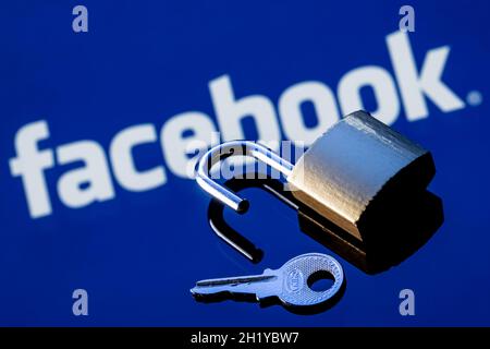 An open security lock and key on the background of the facebook social network logo in the mirror reflection. Stock Photo