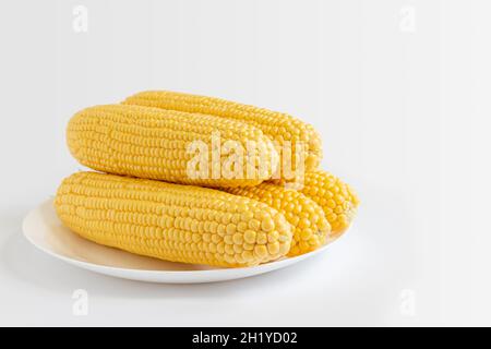 five corn cobs on plate isolated on white background, corn dish, vegetarian food, side view Stock Photo
