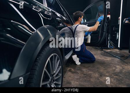 Man in repair workshop washing car window during car valeting Stock Photo