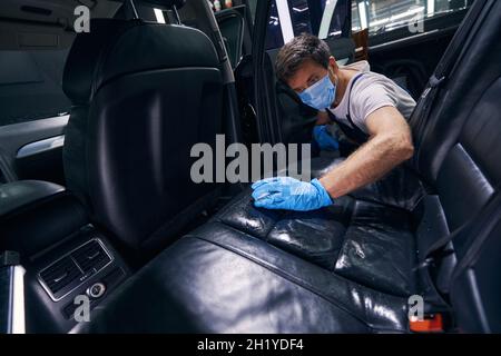 Masked car station worker washing car passenger seats Stock Photo