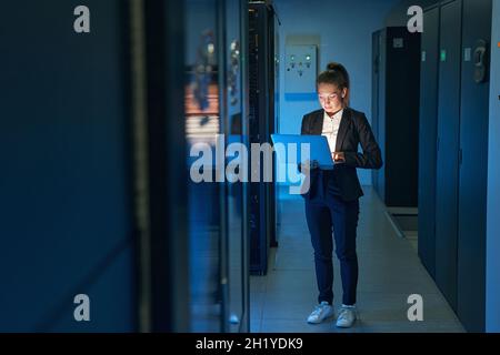 Female technician using laptop to analyze server in data center Stock Photo