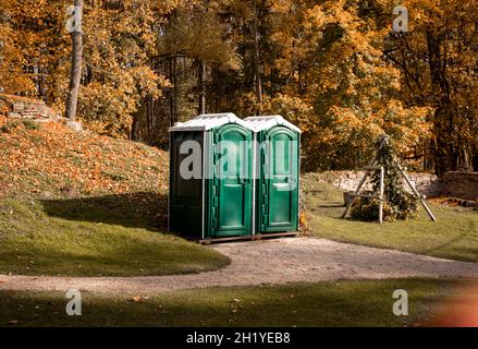 Two portable green toilet cabins in park at dry sunny autumn day Stock Photo