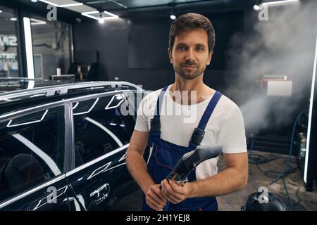 Pleased car technician standing with turned-on steam cleaner Stock Photo