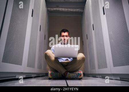 Pleased system administrator working on laptop in server room Stock Photo