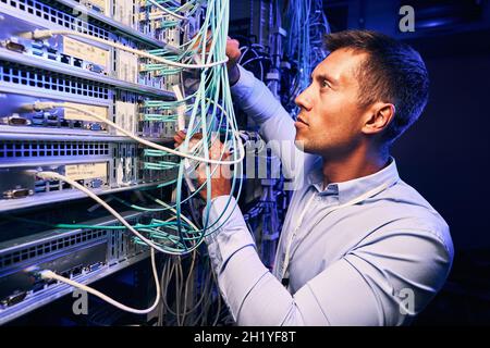 Skilled focused system administrator inspecting fiberl cabling Stock Photo