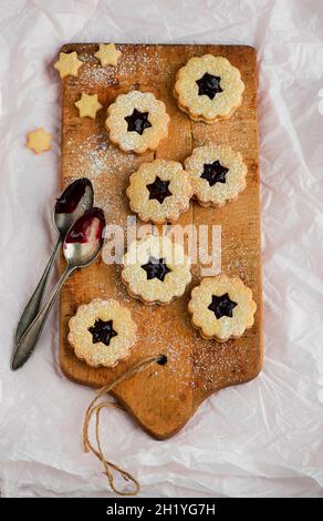 Linzer Plätzchen (nutty shortcrust jam sandwich biscuits with holes on top) on a wooden board Stock Photo