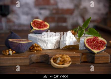 Cheese with white mold and figs lie on a cutting board on a wooden background. Stock Photo