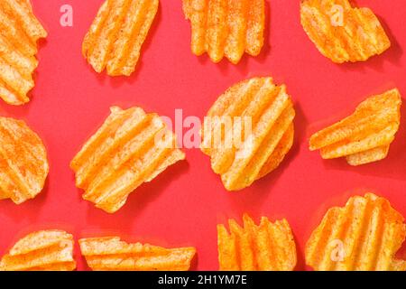 Ribbed potatoes snack with pepper on red background. Ridged potato chips on red background. Set of potato chips. Flat lay. Close-up Stock Photo