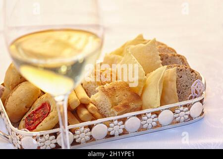 Bread and pastries on a tray in front of a glass of white wine Stock Photo