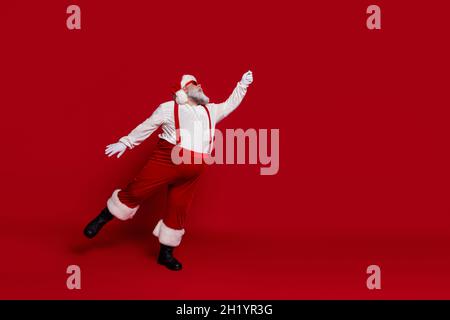 Photo of dreamy carefree old man hold imaginary umbrella wear santa hat suspenders isolated red color background Stock Photo