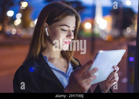 Young Caucasian woman using tablet at night in city Stock Photo