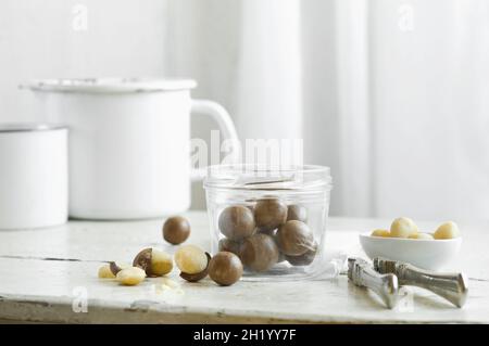 Macadamia nuts in a glass jar and a nutcracker on a rustic kitchen table Stock Photo