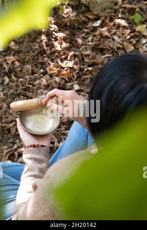 Top vertical view of young woman playing on a Tibetan singing bowl for sound therapy in the nature. Stock Photo