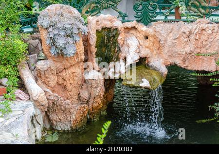 Beautiful artificial waterfall with flowers in the backyard of Ravadinivo Castle, Bulgaria. Stock Photo