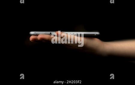 Female hand with mobile phone on a black background. Concept of presentation, mockup and template for modern technology, web network etc. Stock Photo
