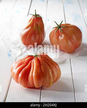 Three beefsteak tomatoes on a white wooden surface Stock Photo