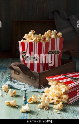 Two red and white striped boxes of popcorn on a wooden tray one box tipped over with popcorn spilling out onto an aqua green blue wooden surface Stock Photo