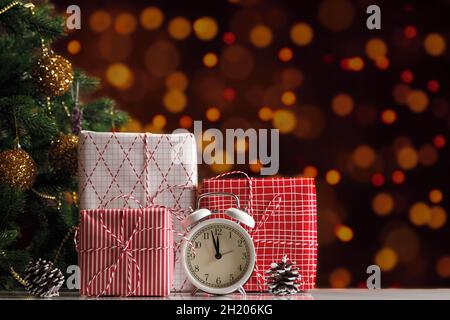 Christmas gift boxes and alarm clock on blurred background of New Year lights. Stock Photo