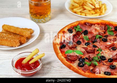 Pizza on a platter close-up on a white wooden table with ketchup, juice, sauce and potatoes. Stock Photo