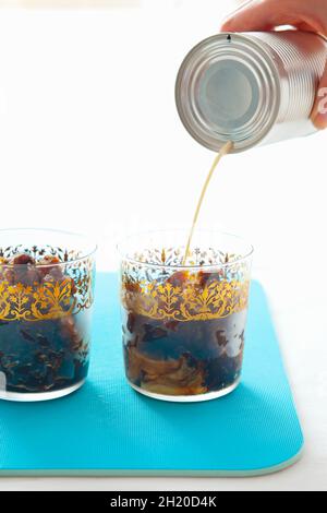 Condensed milk being poured into iced coffee Stock Photo