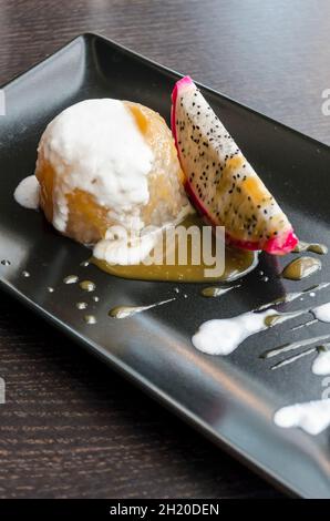 Thai rice pudding with mango and coconut coulis and a slice of dragonfruit on a black plate and dark wooden table Stock Photo