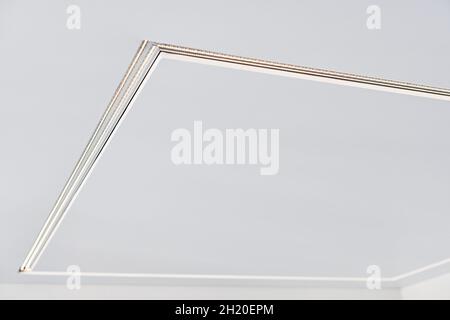 Suspended ceiling with square LED strip lamp in empty room in apartment or house. White stretch ceiling with matte grainy texture. Home renovation con Stock Photo