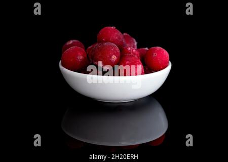 Several berries of red freshly frozen cranberries in a white ceramic bowl, close-up, isolated on black. Stock Photo