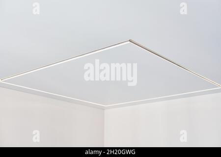 Suspended ceiling with square LED strip lamp in empty room in apartment or house. White stretch ceiling with matte grainy texture. Home renovation con Stock Photo