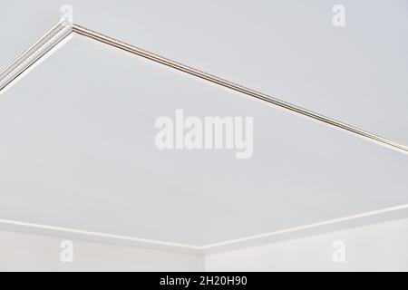 Suspended ceiling with square LED strip lamp in empty room in apartment or house. White stretch ceiling with matte grainy texture. Home renovation con Stock Photo
