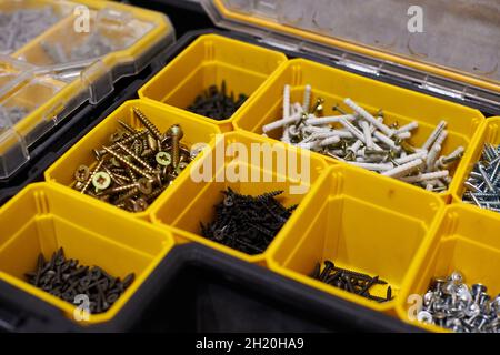 Yellow case with small construction objects. Many storage compartments filled with builders accessories containing screws, nuts, bolts, nails and othe Stock Photo