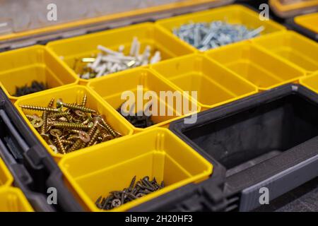 Yellow case with small construction objects. Many storage compartments filled with builders accessories containing screws, nuts, bolts, nails and othe Stock Photo