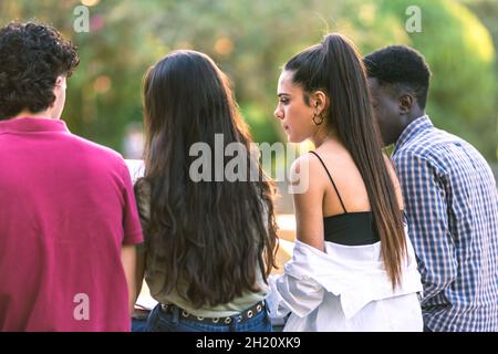 Back of a multiethnic group of students sitting on a bench outdoors studying Stock Photo