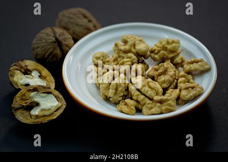 Young grains of walnut top view. Walnuts peeled and in shell on a black background. brown nuts, whole. Walnut kernels in a plate. Stock Photo