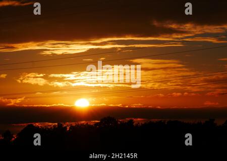 high voltage power lines in the sunlight of the setting sun behind clouds Stock Photo