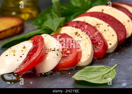 Mozzarella and tomato slices on black slate with basil and spices Stock Photo