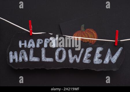 The words Happy Halloween on a black piece of paper hanging on a clothes line. Black Background. Close up. Stock Photo