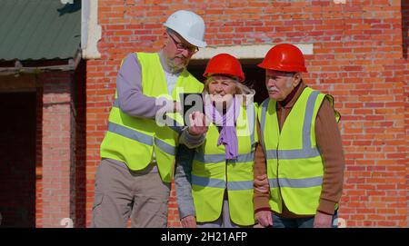 Real-estate agent selling new house to senior grandmother grandfather, showing blueprints on tablet Stock Photo