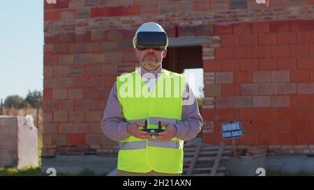 Professional builder drone operator in virtual reality helmet standing in front of construction site Stock Photo