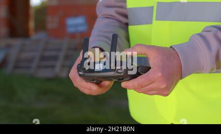 Drone operator holding remote controller controls an aircraft in front of construction house site Stock Photo