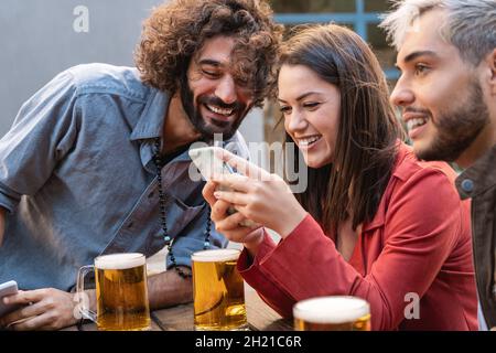 Young people using mobile phone and having fun drinking beer at brewery bar - Happy friends dinning lifestyle concept Stock Photo