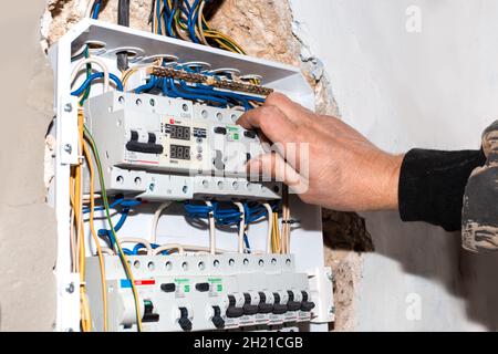 Russia, Anapa-07.11.2020: The electrician turns on the switches of the electrical panel built into the wall of the house. Electricity control device. Stock Photo