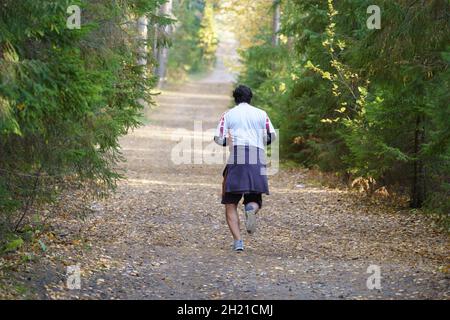 Athlete man jogging in autumn forest. Male runner training outdoors before running marathon in park Stock Photo