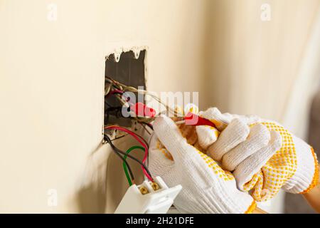 An electrician is replacing a wall switch. A DIY project concept. High voltage danger. The professional wearing shock proof gloves is tightening wiren Stock Photo