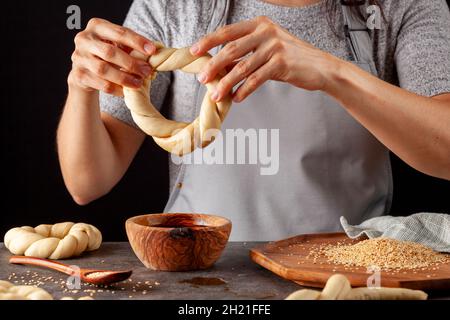 delicious Turkish bagel with sesame seeds known as susamli simit.  Woman baker is making it using twisted dough dipped into a bowl of pekmez and sesam