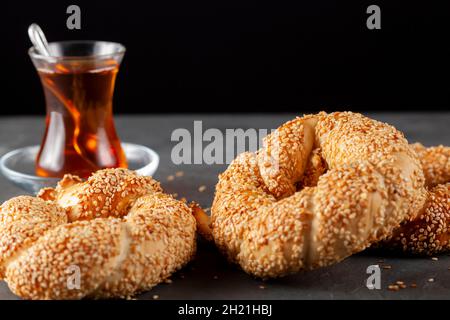delicious Turkish bagel with sesame seeds known as susamli simit. Dark background crumbly fresh out of oven pastry served on stone with a cup of black Stock Photo