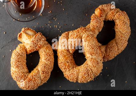 delicious Turkish bagel with sesame seeds known as susamli simit. Flat lay image shows three rolls served with black tea inside glass Turkish tea cups Stock Photo