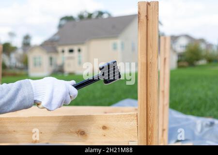 outdoor diy project in backyard with lawn. A person wearing safety gloves is installing a wooden fence or furniture using a plastic hammer to tighten. Stock Photo