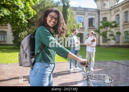 A smiling young mulatta riding a bike and feeling cheerful Stock Photo