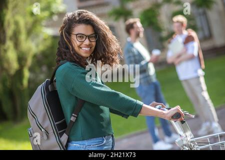 A smiling young mulatta riding a bike and feeling cheerful Stock Photo
